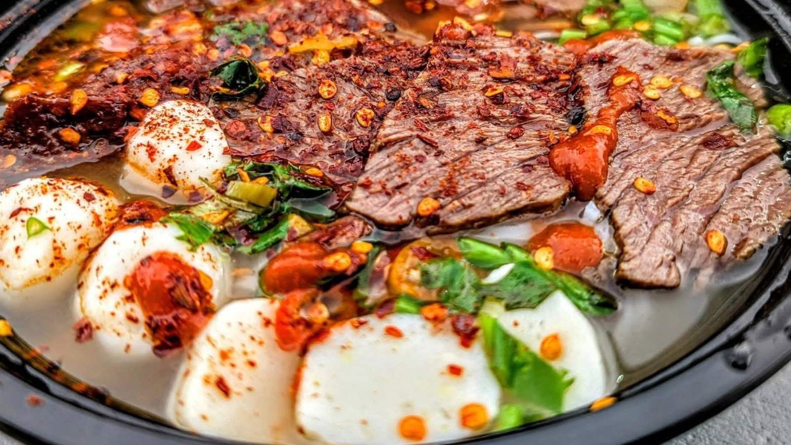 Sliced beef over noodles with herbs, chili and pale rounds of fish cake. Photograph posted by Hasina's Burmese Kitchen.