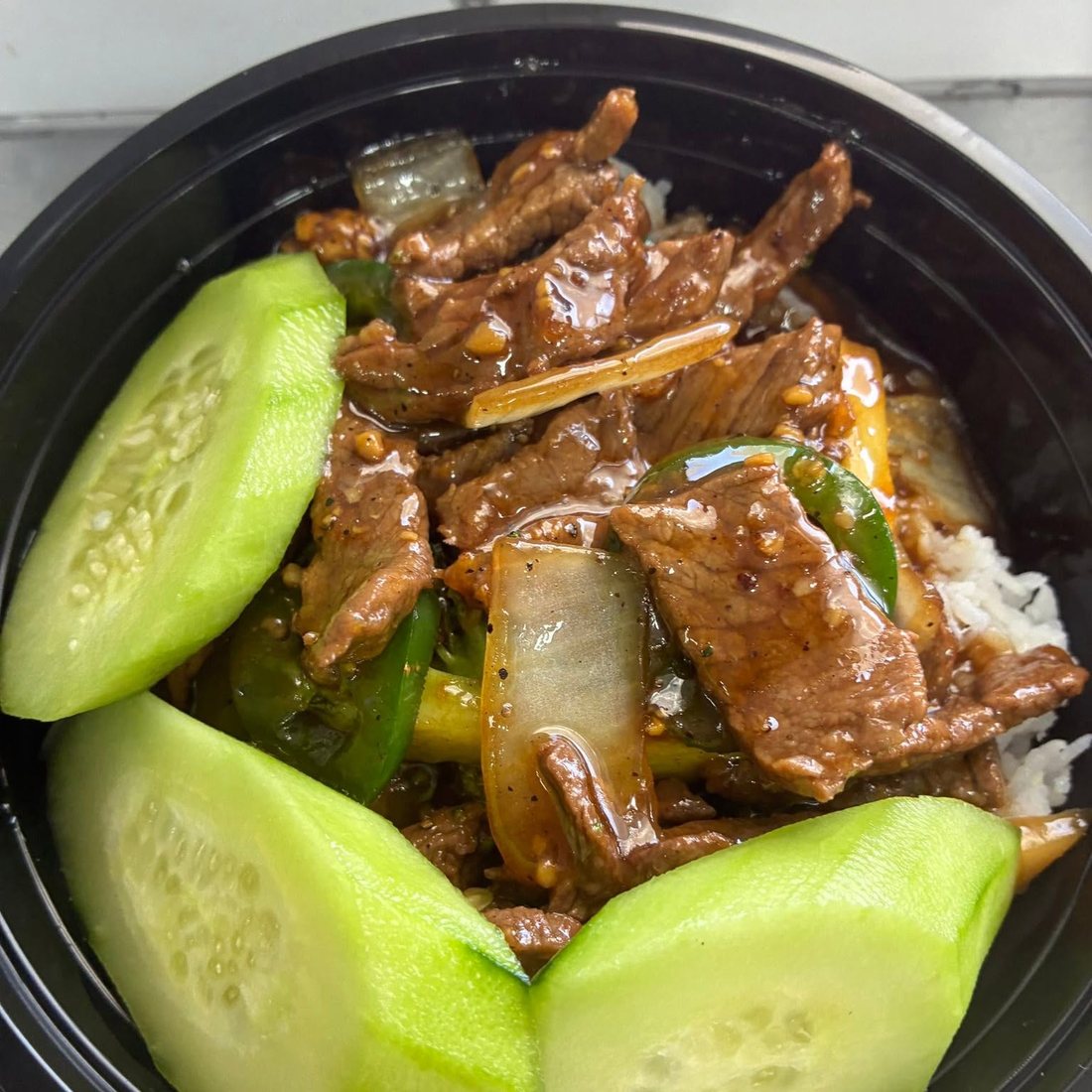 Beef and peppers in a dark sauce over rice, with slices of cucumber. Photograph posted by Hasina's Burmese Kitchen.