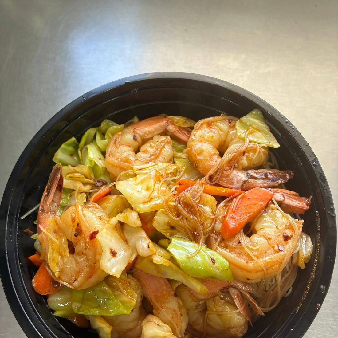 Shrimp stir-fried with cabbage, carrot and noodles in a black bowl. Photograph posted by Hasina's Burmese Kitchen.