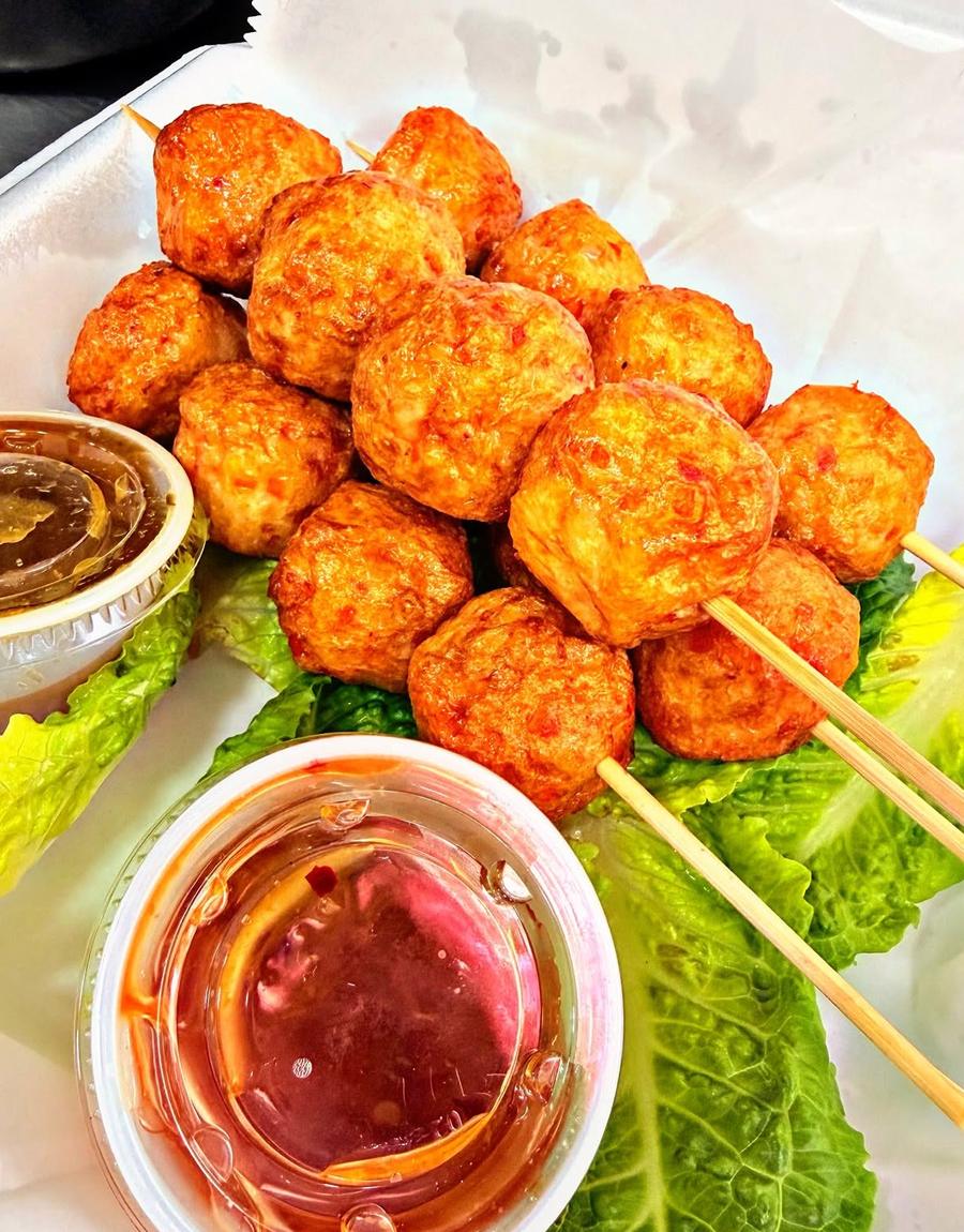 A row of skewers laid over lettuce with two cups of dipping sauce. Photograph posted by Hasina's Burmese Kitchen.