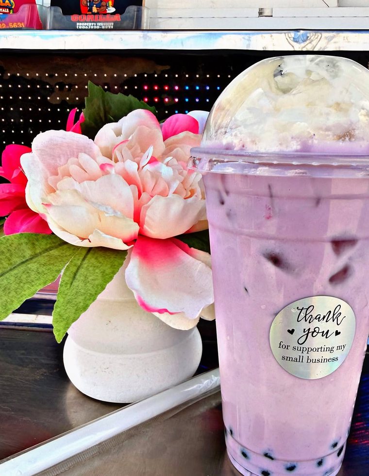 A tall purple boba drink beside a flower on the counter. Photograph posted by Hasina's Burmese Kitchen.